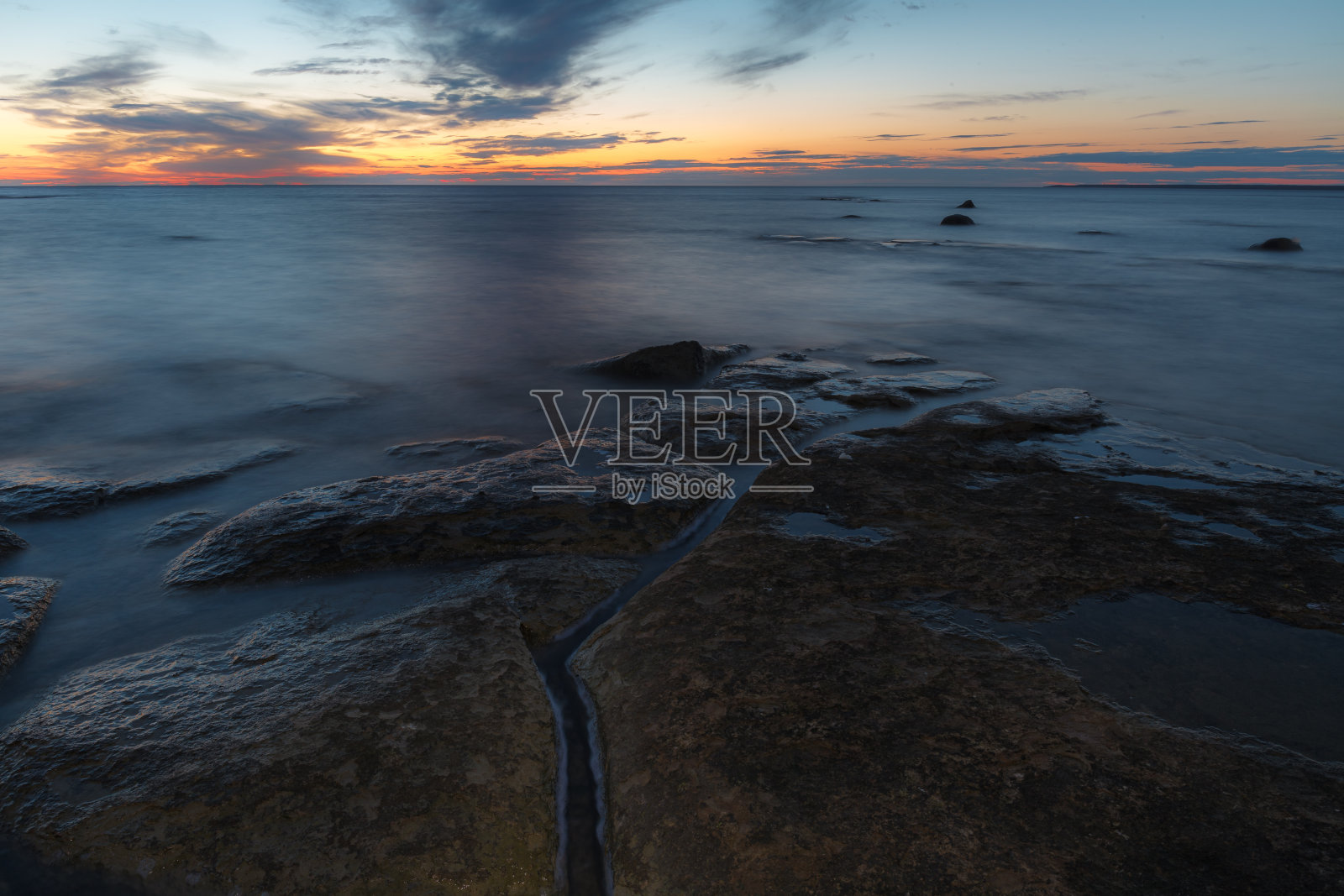 波罗的海岩石海岸的黄昏日落。几乎晴朗的天空和橙色的带子沿horison。爱沙尼亚。照片摄影图片