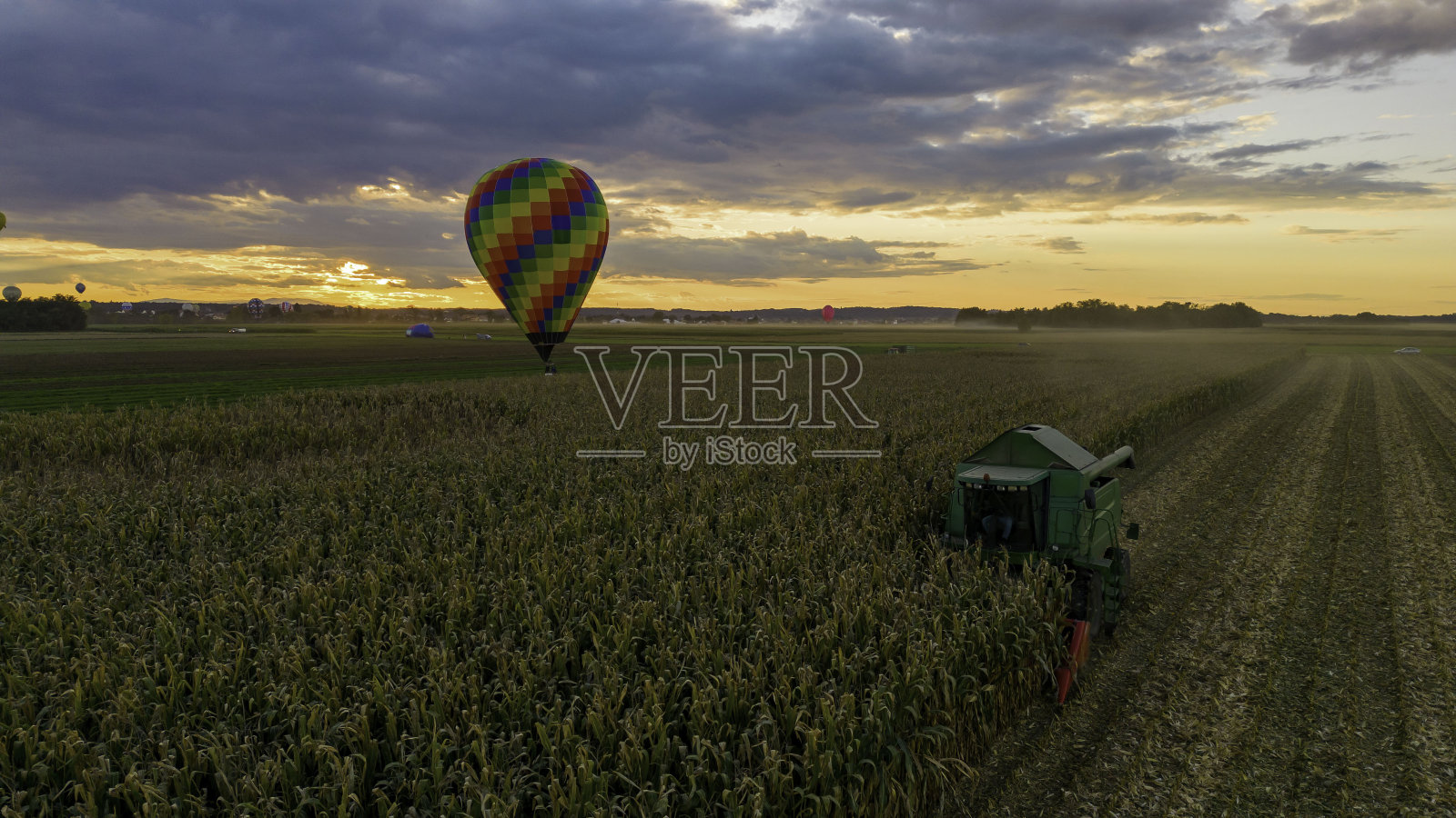 鸟瞰收割玉米的联合收割机，日落时站在农田旁的热气球照片摄影图片