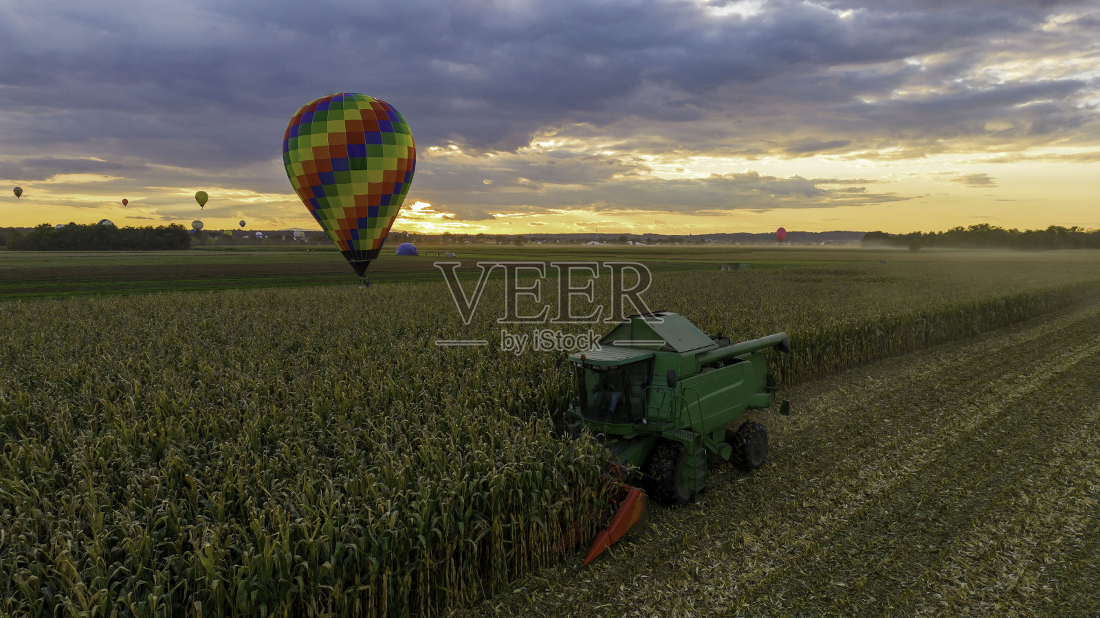 鸟瞰图日落时分，联合收割机正在割玉米，热气球站在田地后面，多个热气球在天空中翱翔照片摄影图片