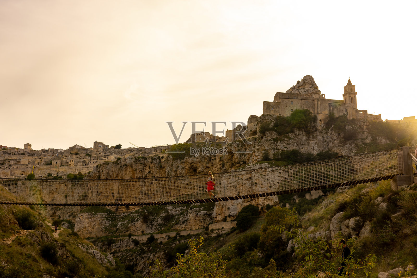 游客走在绳索人行桥上的树木与城市的背景照片摄影图片