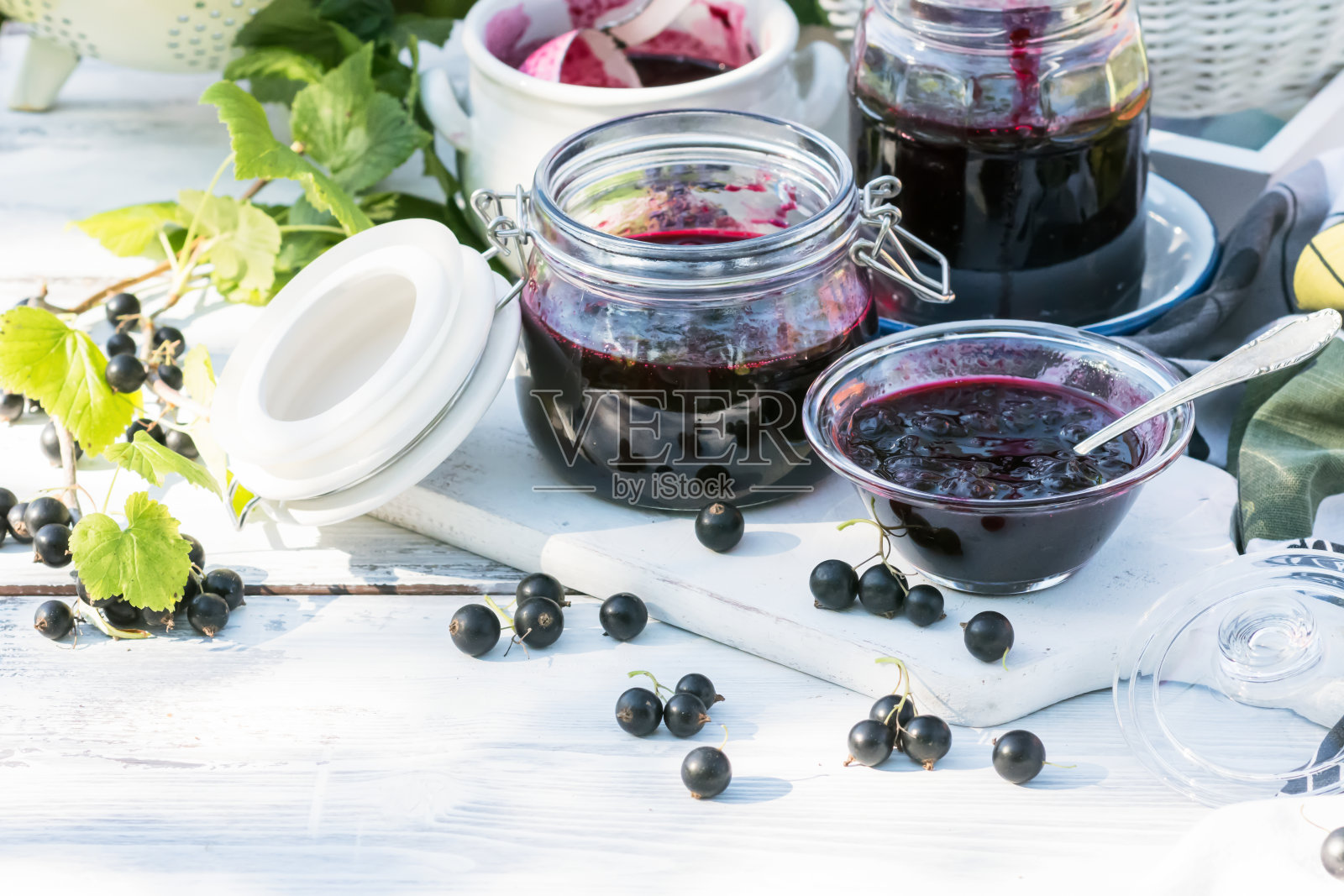 自制熟黑加仑果酱放在小玻璃碗和白色木桌上的罐子里，新鲜黑加仑果酱靠近照片摄影图片