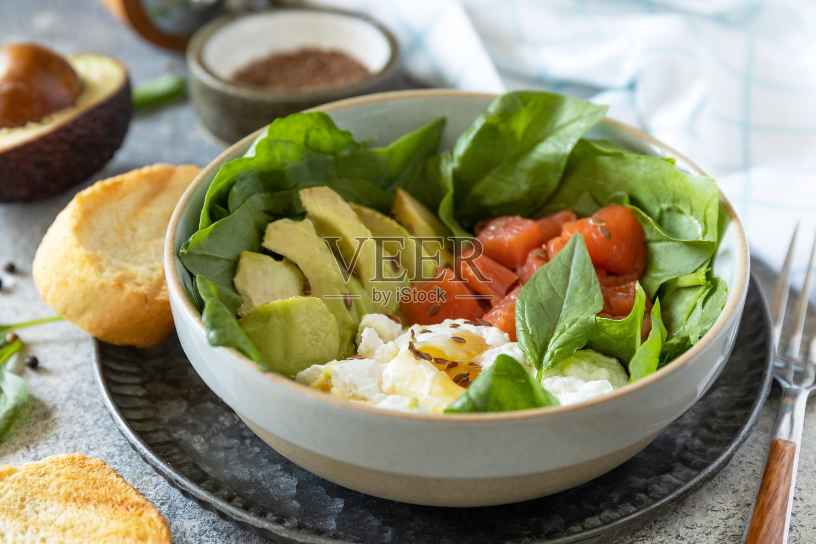 经典的早餐，早午餐——水煮蛋，牛油果，芝麻菜，亚麻籽和盐腌鲑鱼在灰色的背景上。照片摄影图片