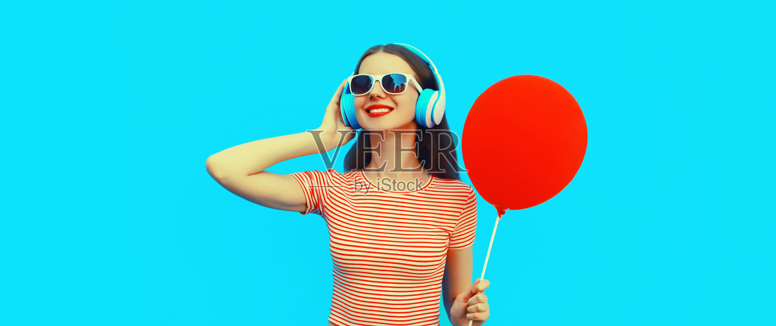 肖像快乐微笑的年轻女子气球耳机听音乐在蓝色背景照片摄影图片
