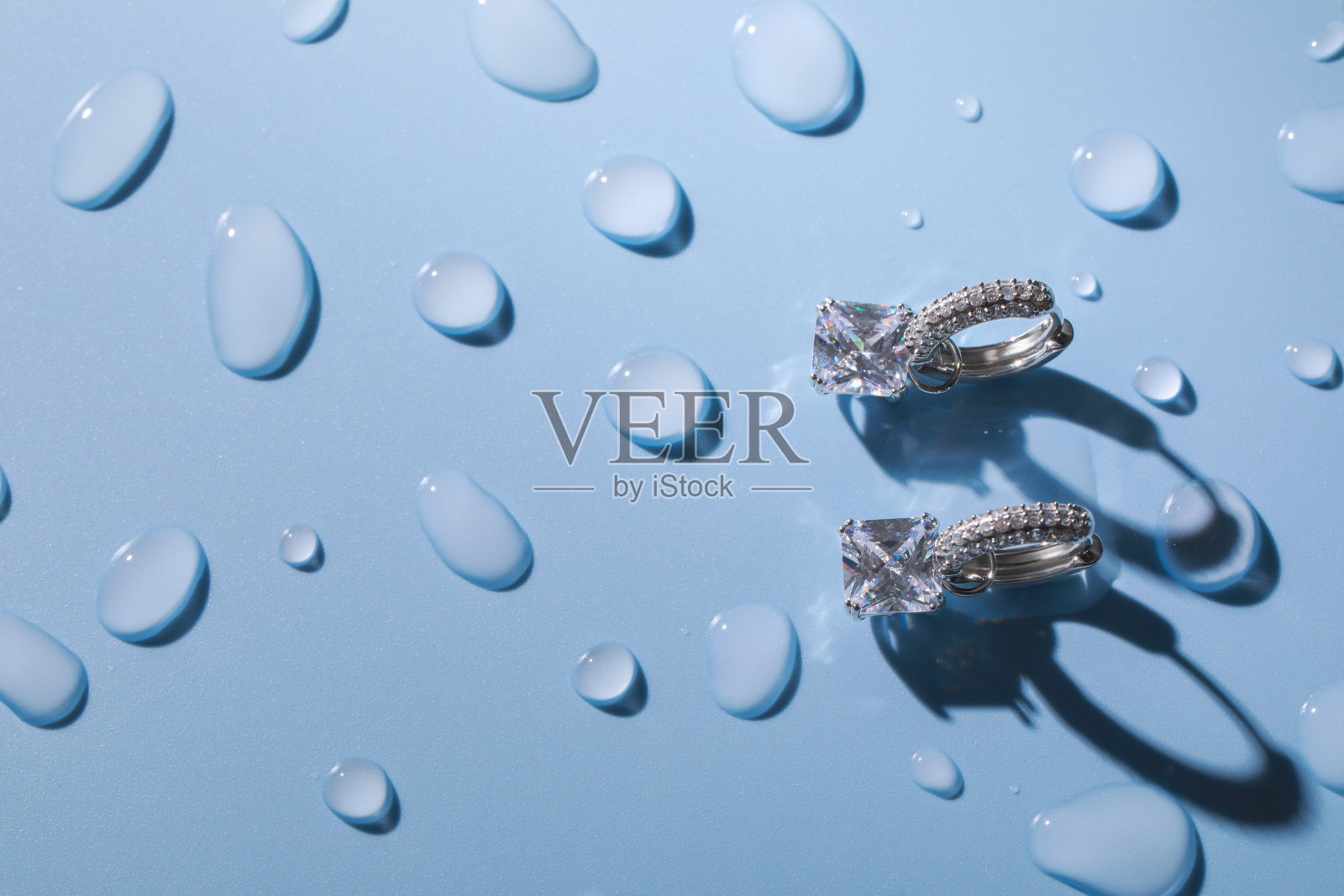 奢华的珠宝。优雅的耳环在浅蓝色表面覆盖着水滴，平坦的铺设和文字空间照片摄影图片