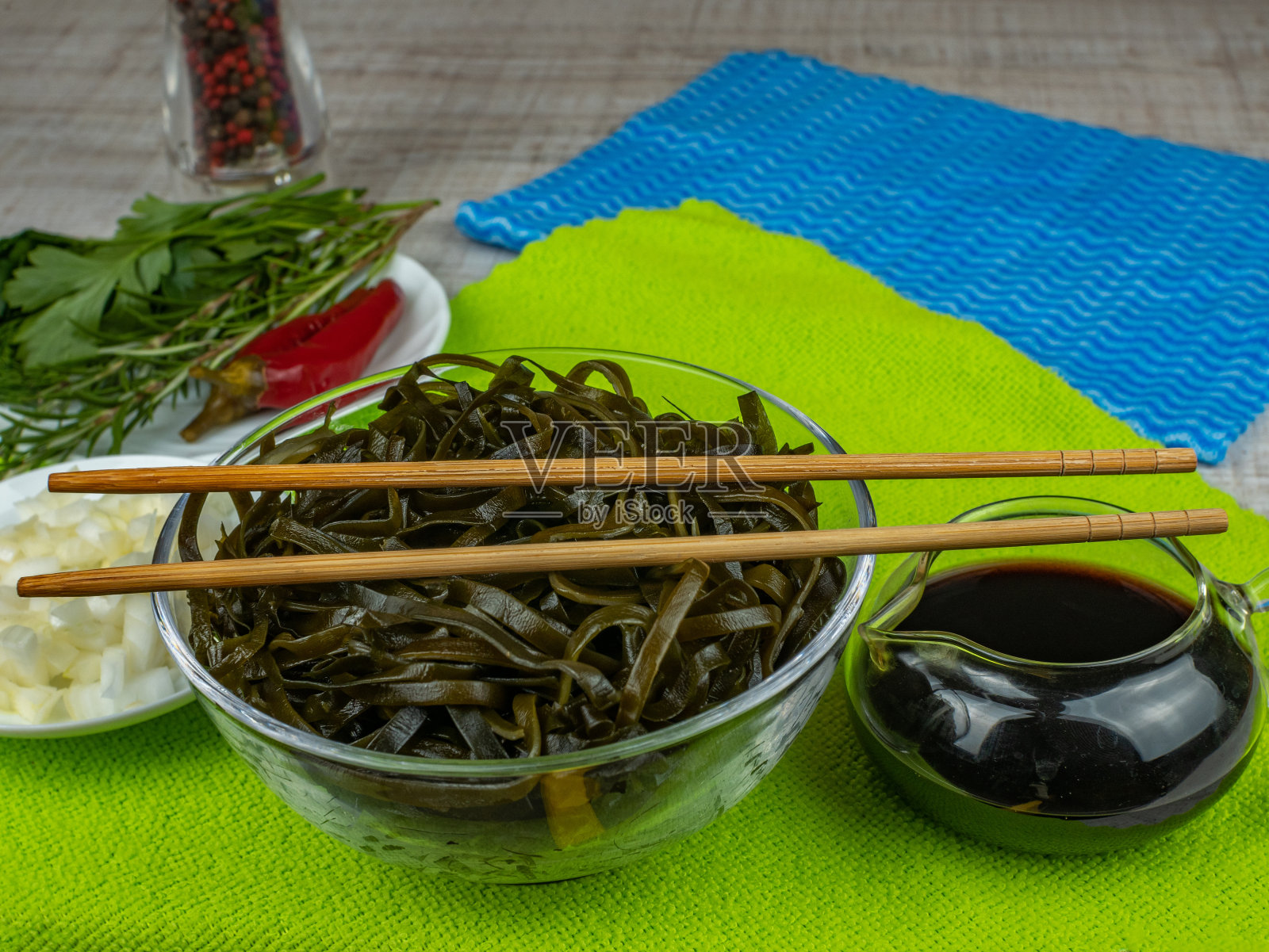海带沙拉配洋葱和酱油，碗和木筷子。绿色餐巾纸上有一碗紫菜沙拉、盛着红辣椒、香草的碟子和盛有酱油的肉汁碗照片摄影图片