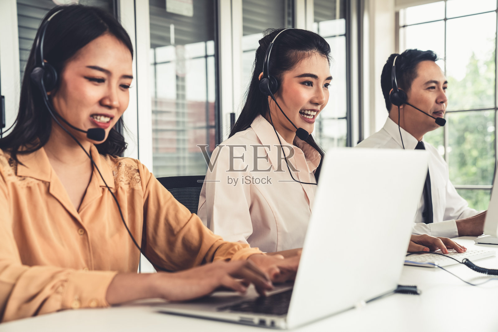 商务人士戴着耳机在办公室积极工作。呼叫中心、电话营销、客服为客户提供电话视频会议服务。照片摄影图片