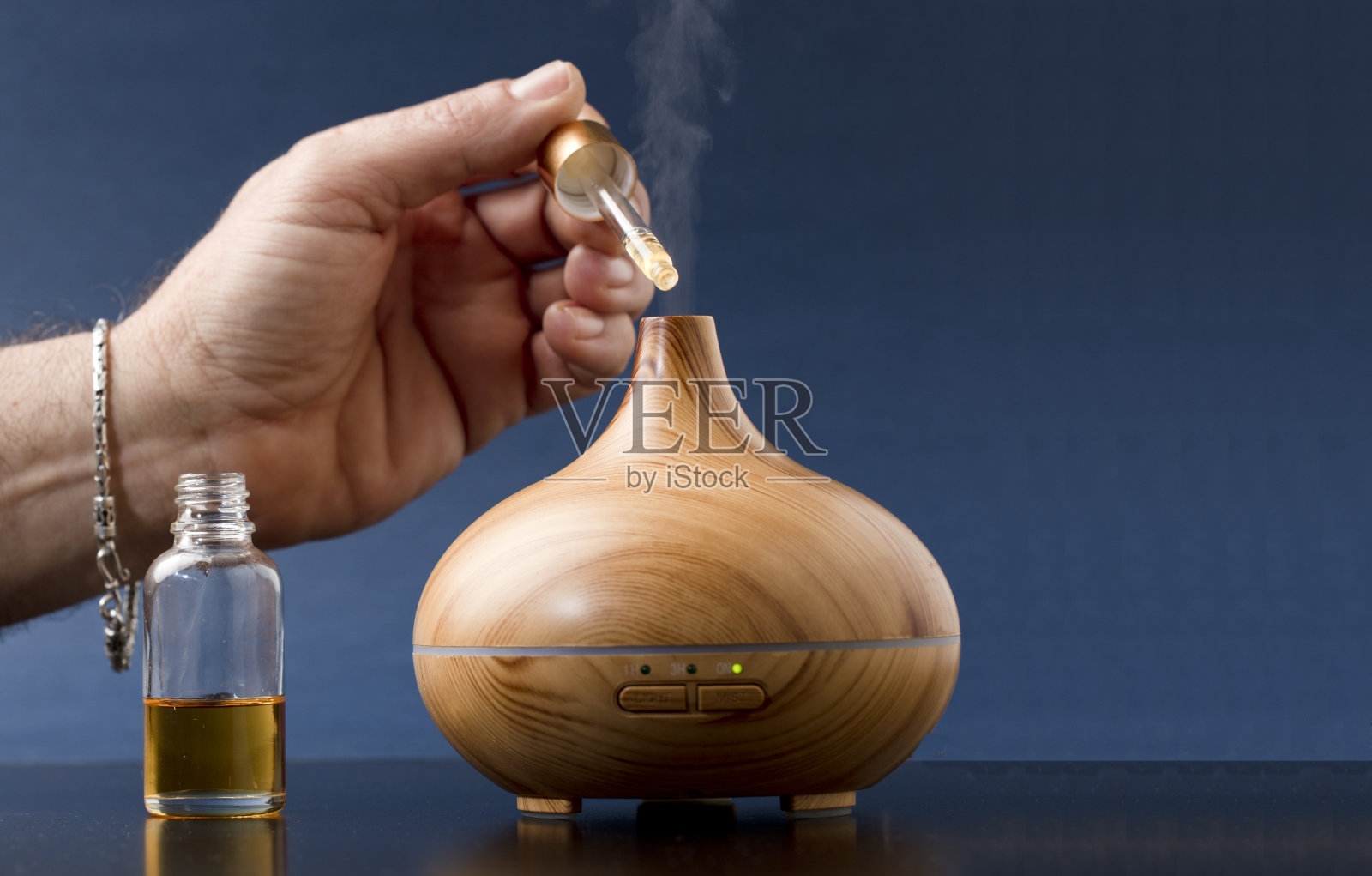 木制空气清新剂与蒸汽的自然精华，男子的手与手镯充电，蓝色背景照片摄影图片