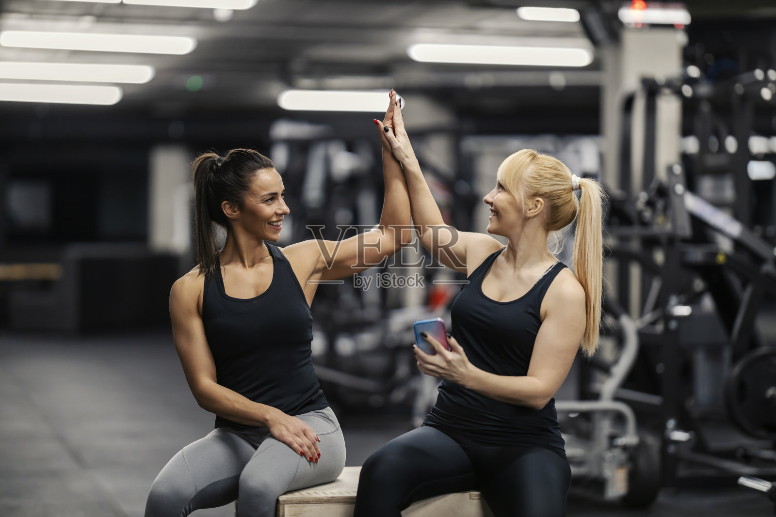 在体育馆里的成就。两个女运动员坐在体育馆里互相击掌。照片摄影图片