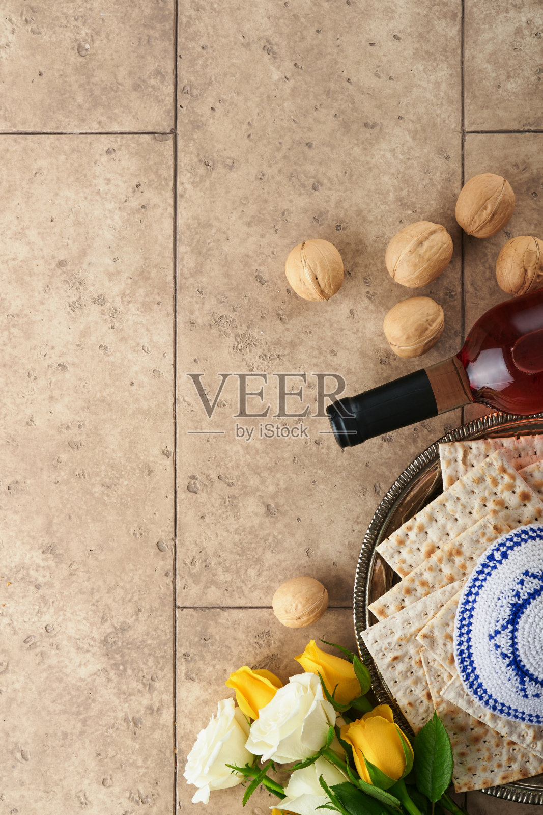 逾越节庆祝概念。无酵饼，犹太红酒，核桃，白玫瑰和黄玫瑰。传统仪式犹太面包上的沙色旧瓦墙背景。逾越节的食物。逾越节是犹太人的节日。照片摄影图片