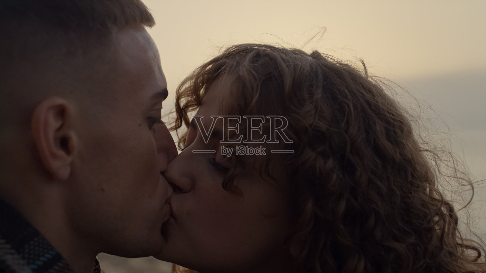 日落时分，情侣在海滩上亲吻。微笑的女人看着男人照片摄影图片