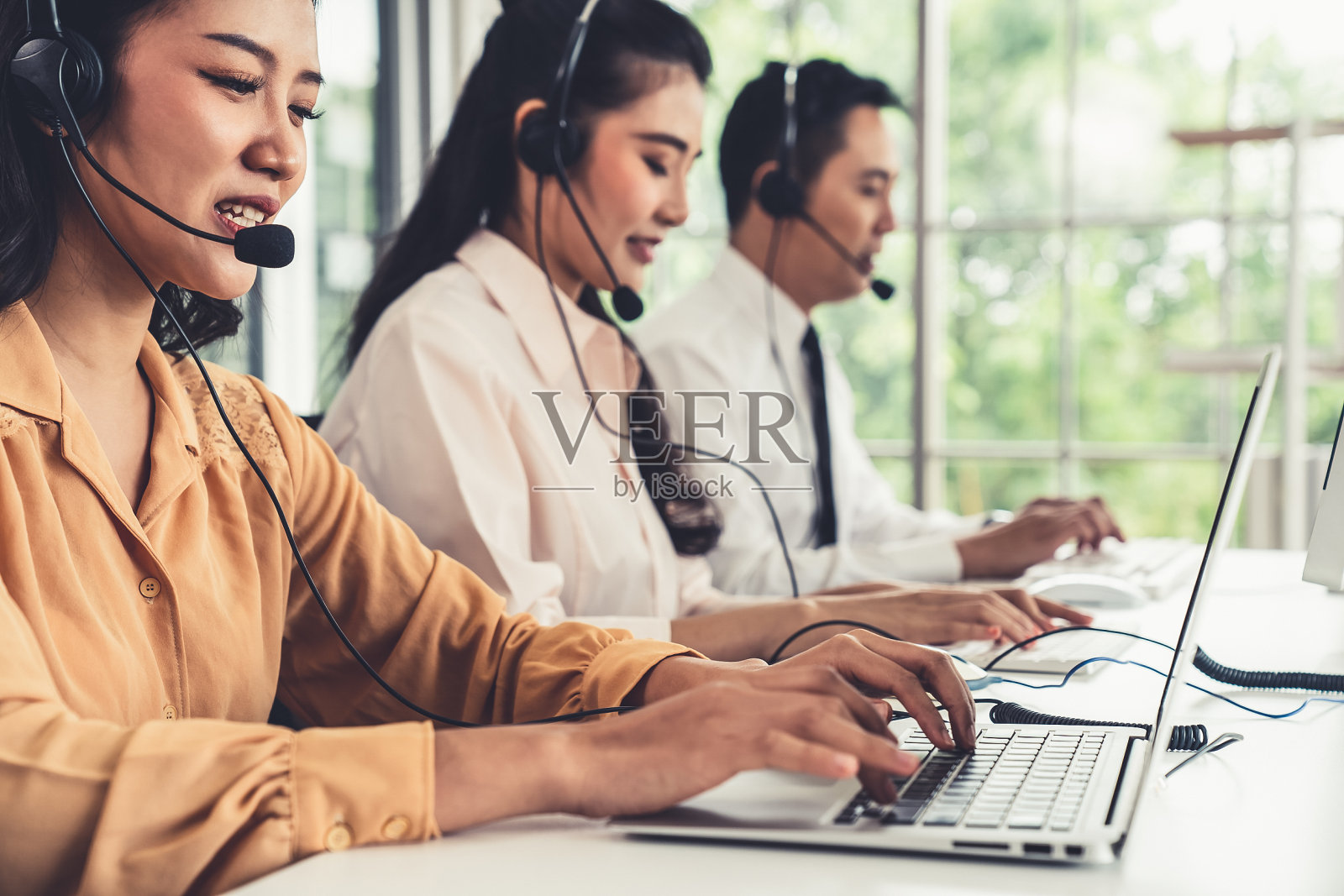 商务人士戴着耳机在办公室积极工作。呼叫中心、电话营销、客服为客户提供电话视频会议服务。照片摄影图片