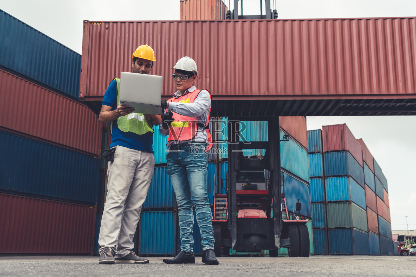 产业工人在海外集装箱堆场与同事一起工作。物流供应链管理与国际货物出口概念。照片摄影图片