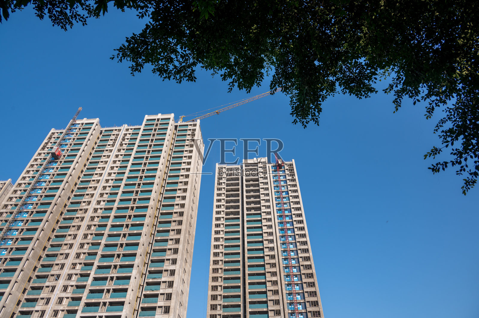 蓝天下未完工的城市建筑和树荫照片摄影图片