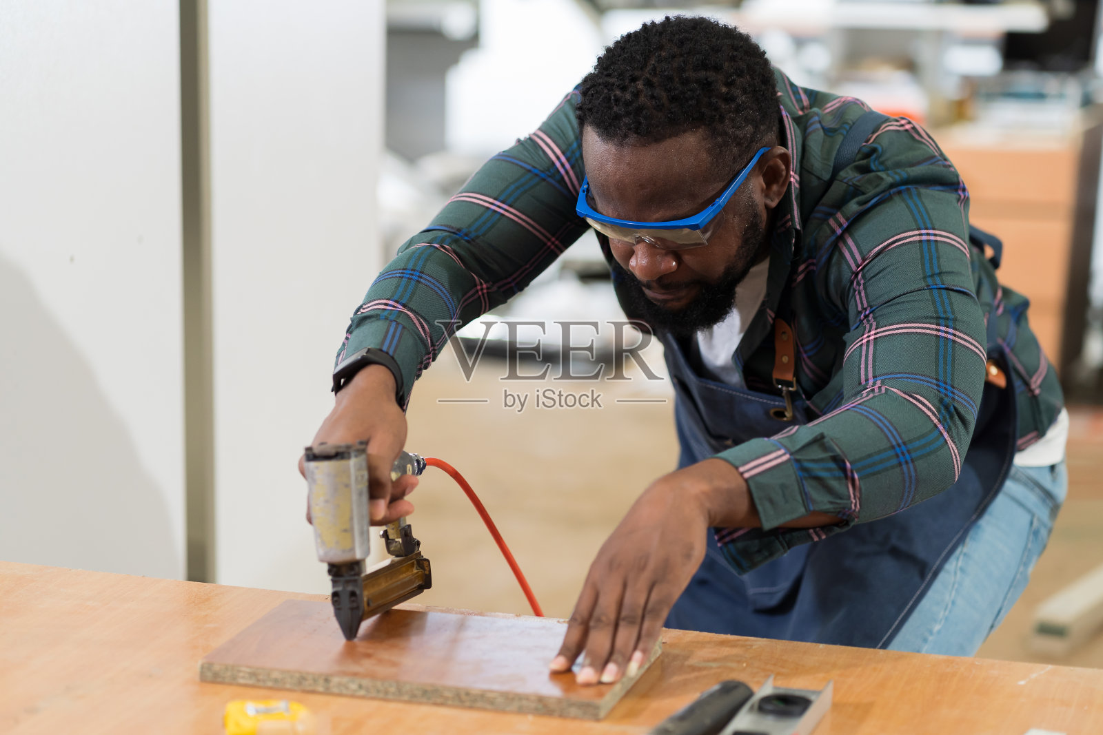 非裔美国男性木匠使用气动钉枪射击木板在木材车间。木工男工人在木材厂用气动钉枪制作新家具照片摄影图片