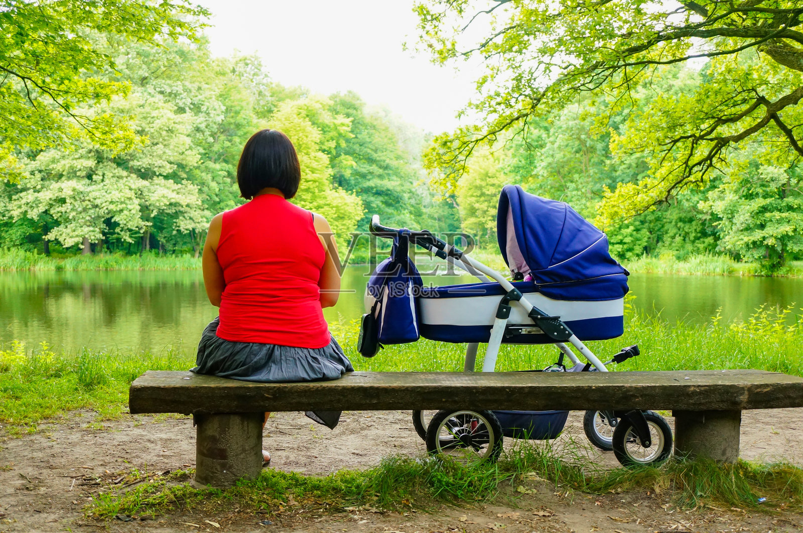一个女人坐在木长椅上，旁边是一辆婴儿车照片摄影图片