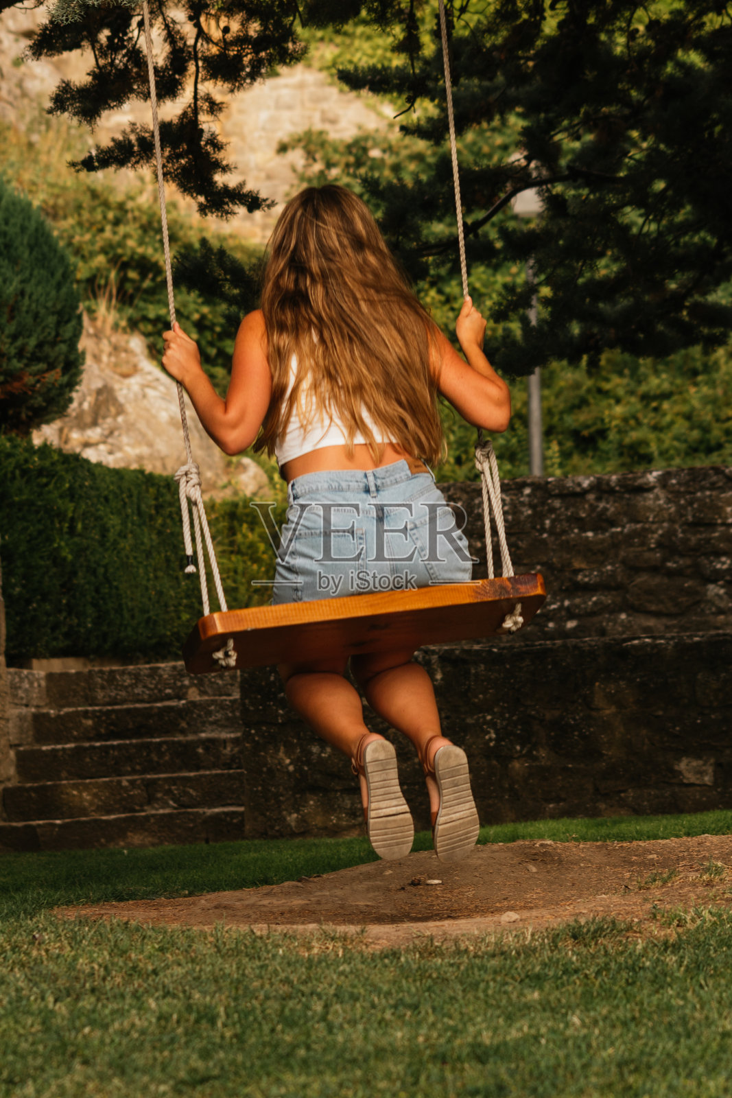 一个白人妇女在花园里荡秋千的背影的垂直镜头照片摄影图片