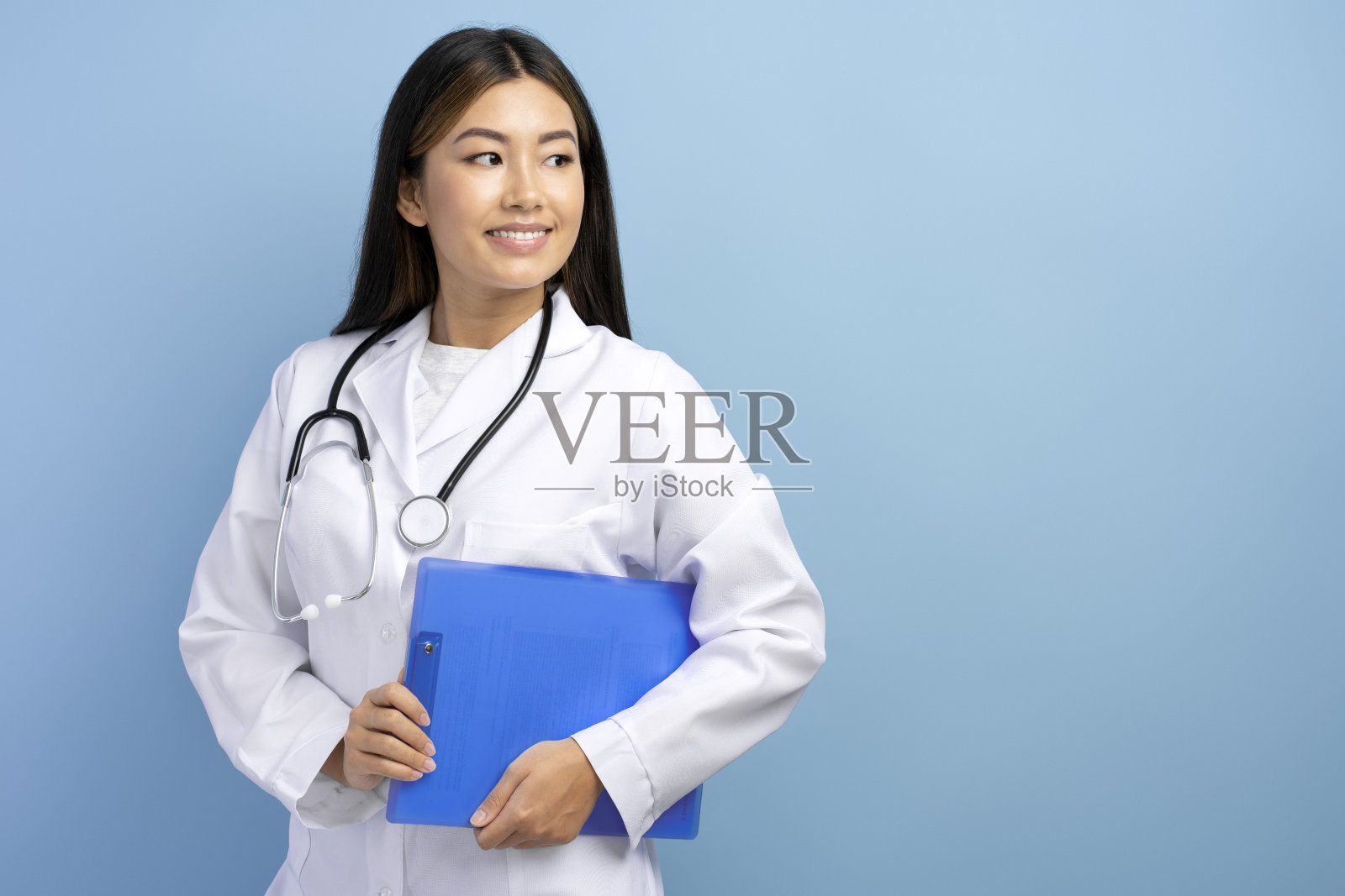 微笑的亚洲女医生儿科穿着白色的医疗袍拿着文件夹，看向别处照片摄影图片