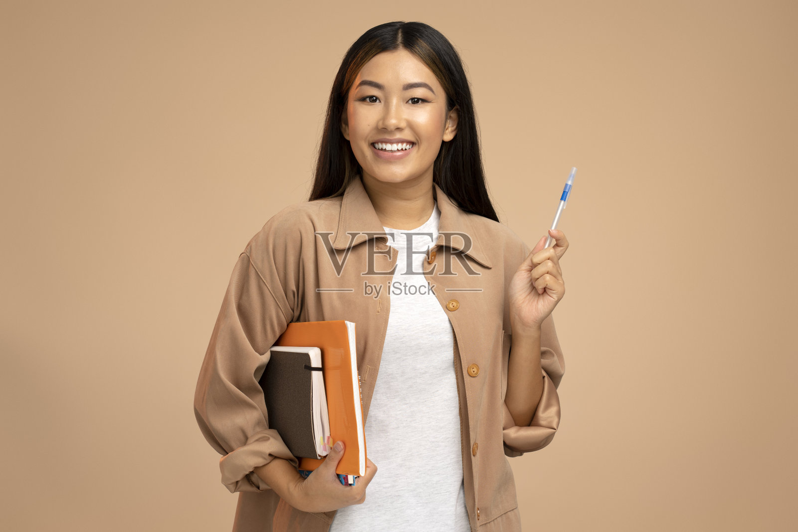 亚裔女学生手里拿着书或纸，微笑着看着镜头照片摄影图片