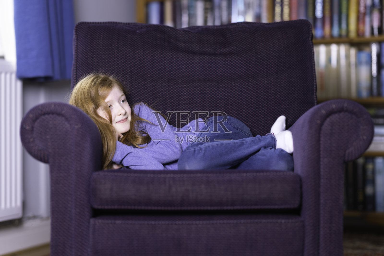 红头发的年轻女孩舒适地蜷缩在扶手椅上照片摄影图片