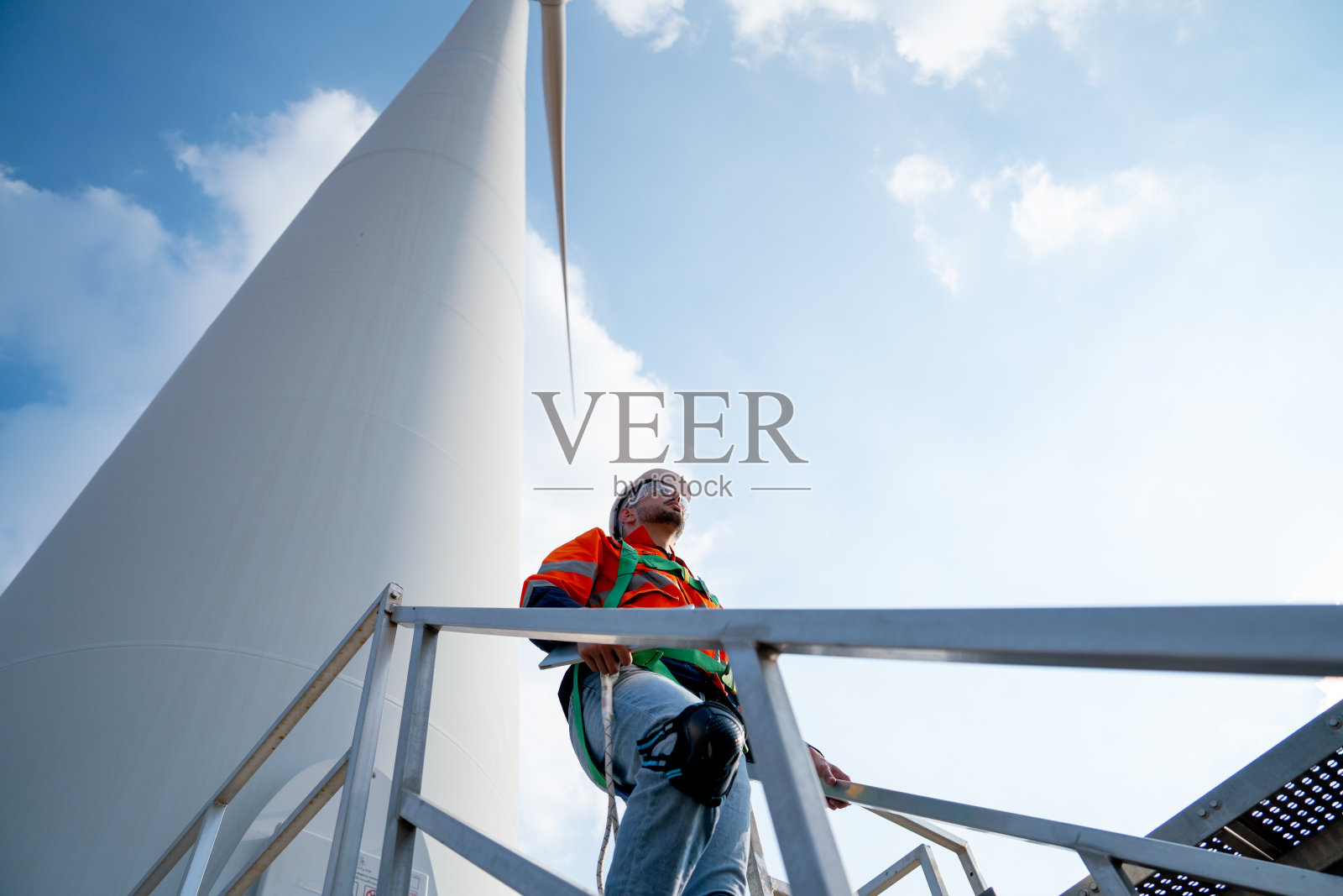 白人工程师或技术工人走在风车或风力涡轮机的底部，展望蓝天和日光。照片摄影图片