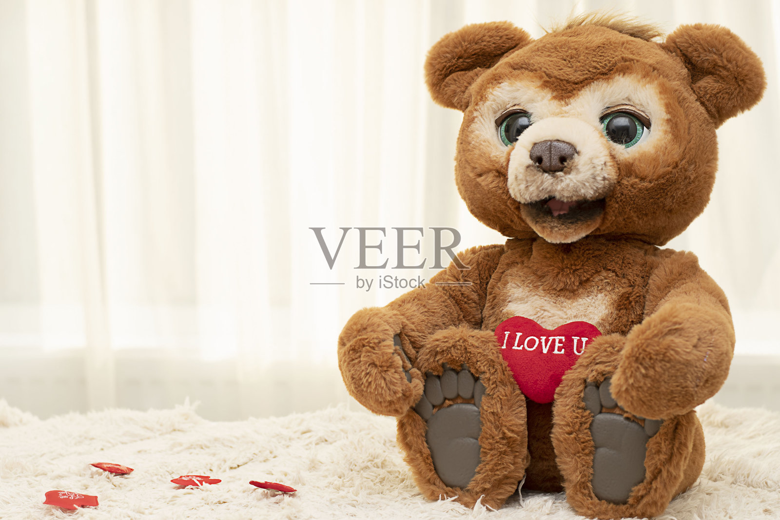 情人节的概念。一只可爱的棕色大眼睛泰迪熊坐在靠窗的地毯上，上面有一颗鲜红色的心。照片摄影图片