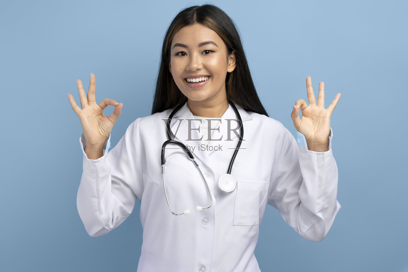 满意的亚洲女医生站在肖像，看着相机显示Ok迹象照片摄影图片