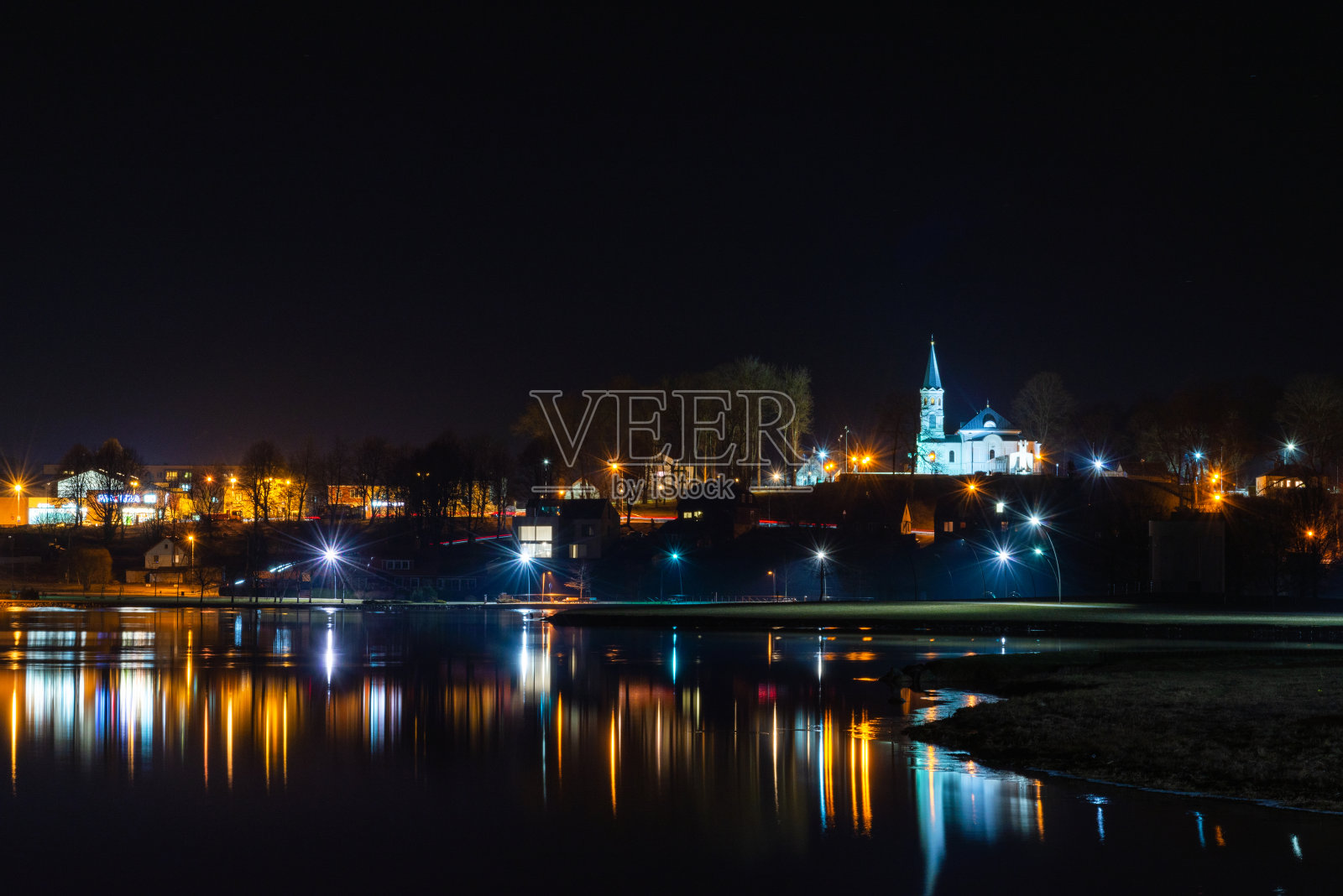 Telsiai镇，立陶宛的水夜湖。美丽的景色冬天五颜六色的房子在结冰的湖海岸。美好的冬夜。小镇五颜六色的灯光映在水面上。长时间的曝光。照片摄影图片