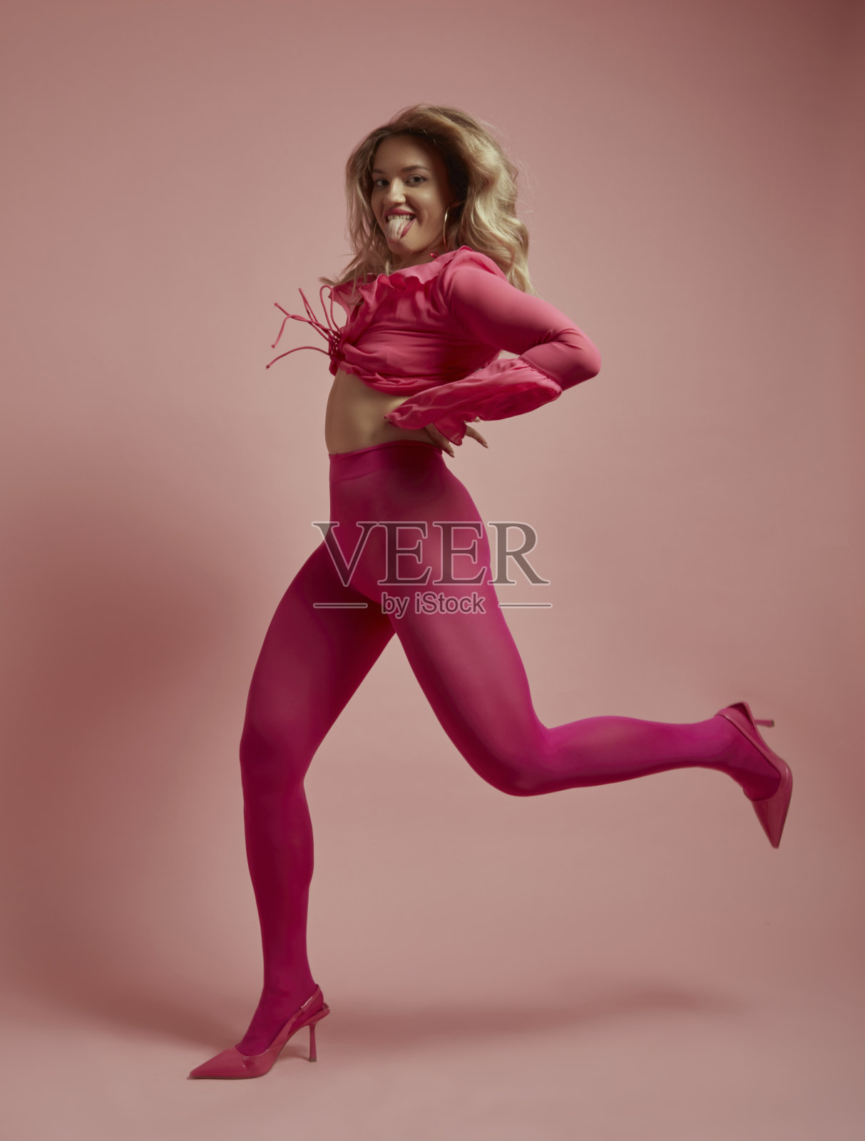 美丽的金发女人在粉红色背景前跳跃。照片摄影图片