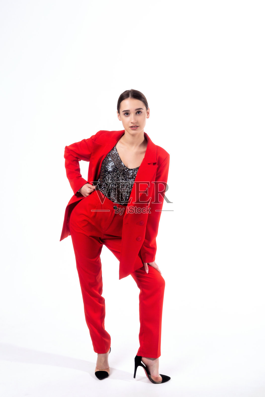 一名穿着红色裤装和闪亮上衣的年轻女子在白色背景下摆姿势。照片摄影图片