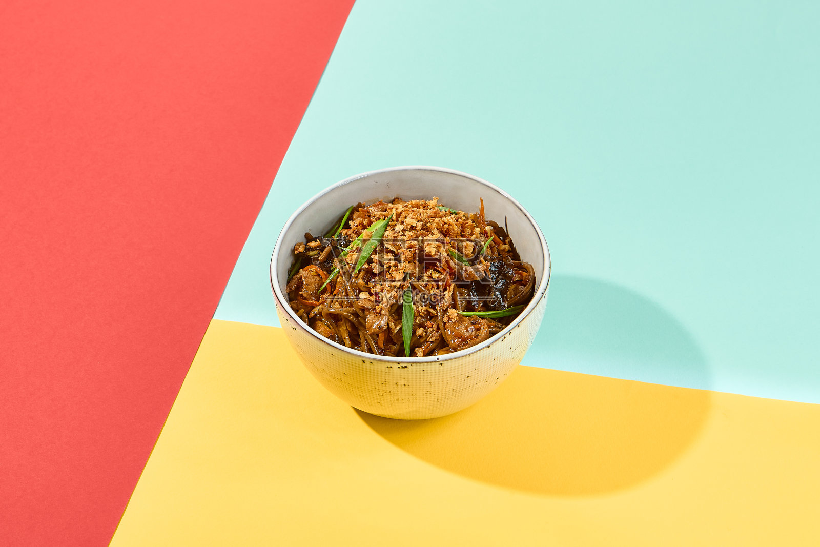 黄、红、蓝三色底色的陶瓷碗炒面。炒荞麦面，有阴影的时尚风格。充满活力的食物照片摄影图片