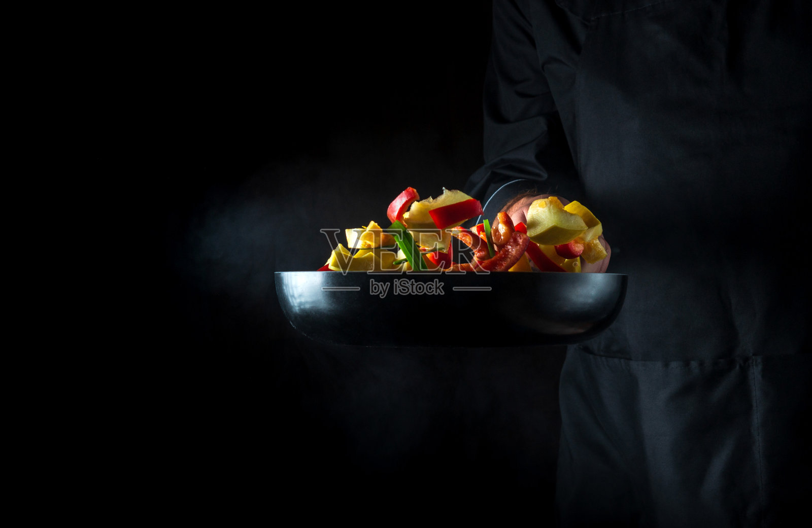 厨师在煎锅里准备蔬菜。在深色背景上烹饪健康的素食食物和餐点。免费广告位。照片摄影图片