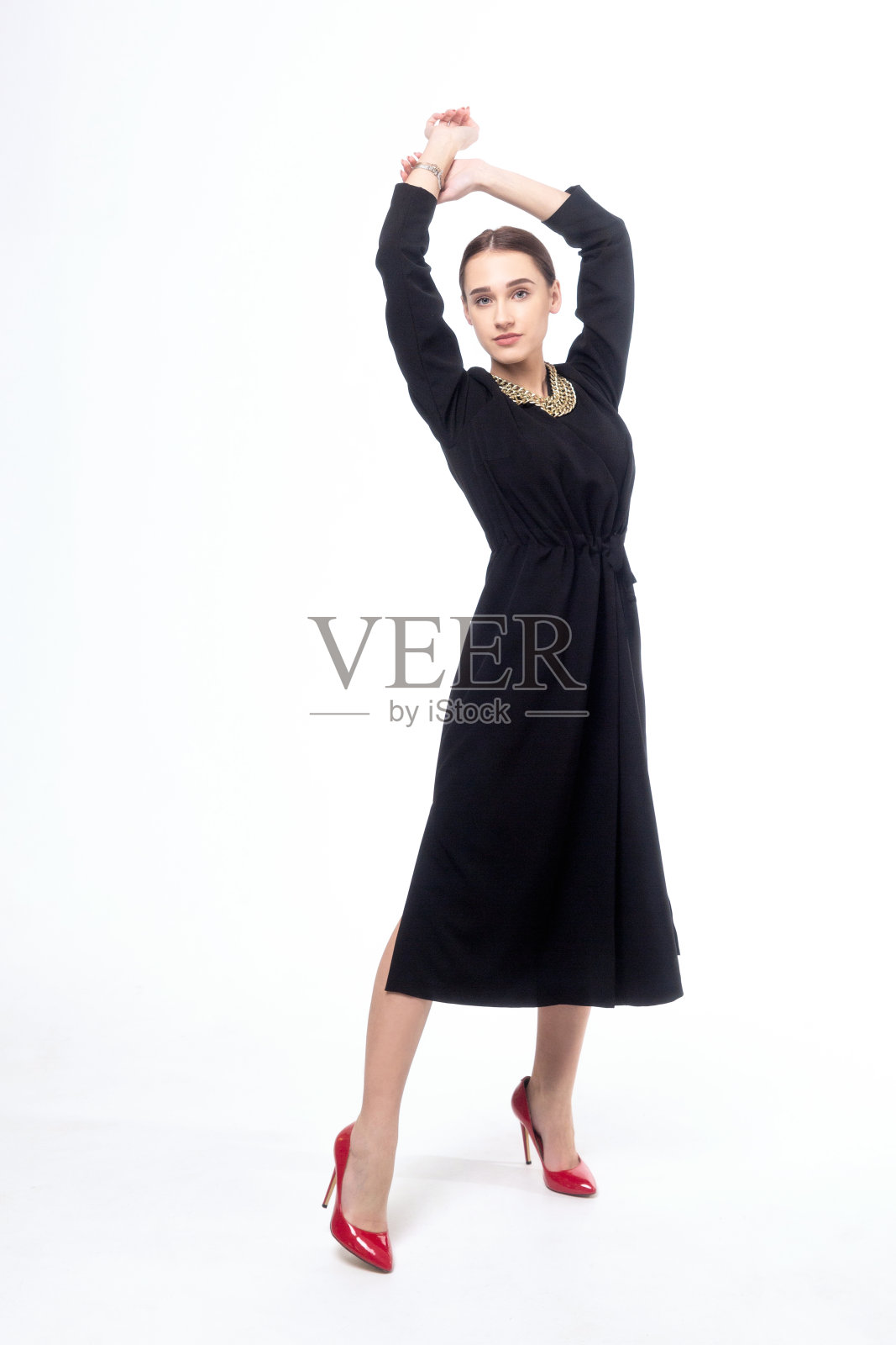 年轻女子在黑色连衣裙和红色鞋子摆姿势在白色背景。照片摄影图片
