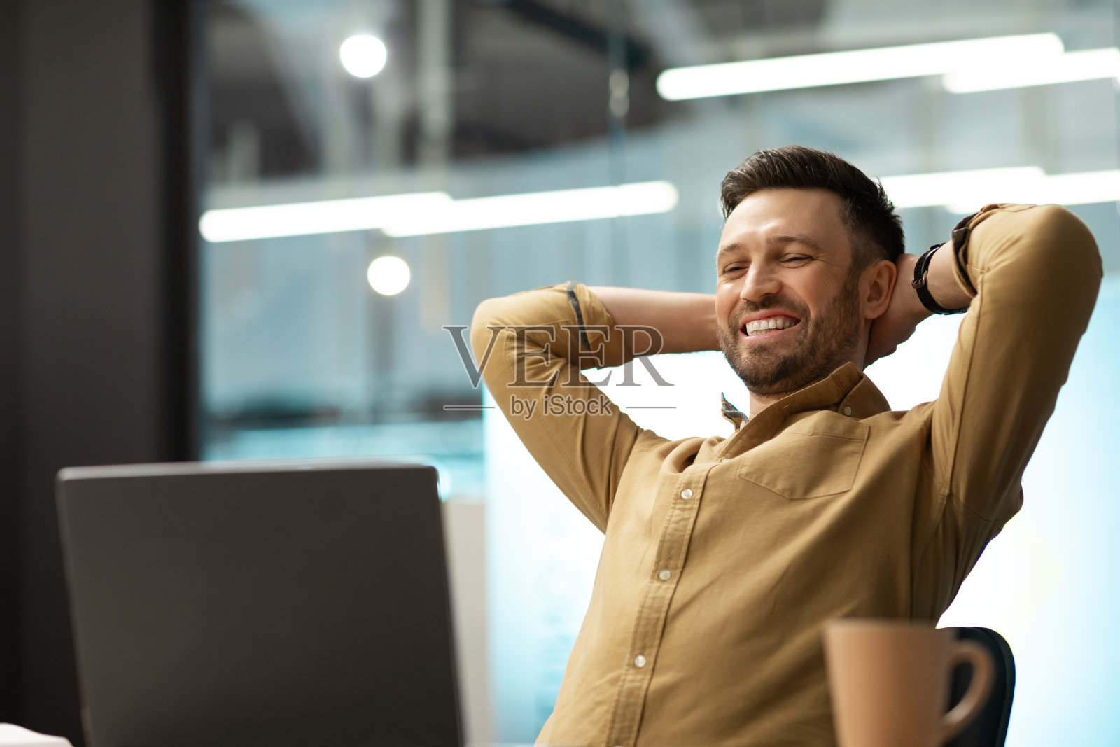 快乐的商人看着笔记本电脑放松坐在办公室照片摄影图片