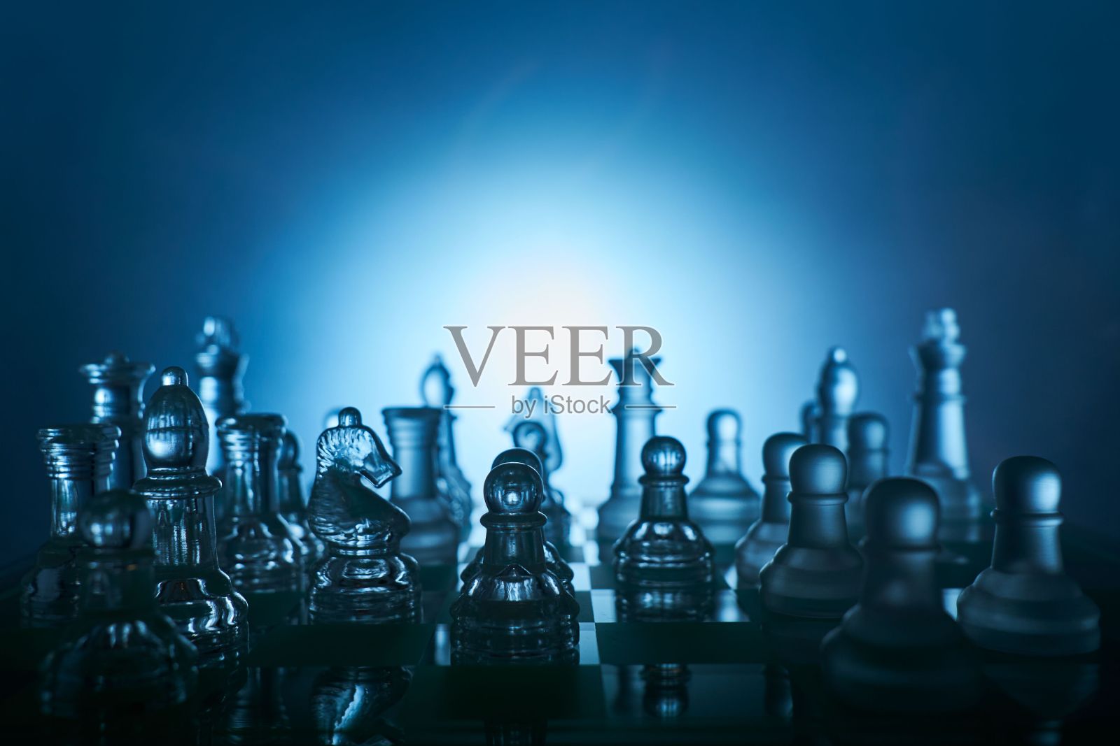 透明的国际象棋人物特写，在国际象棋板与黑暗的环境和蓝色的背景。照片摄影图片