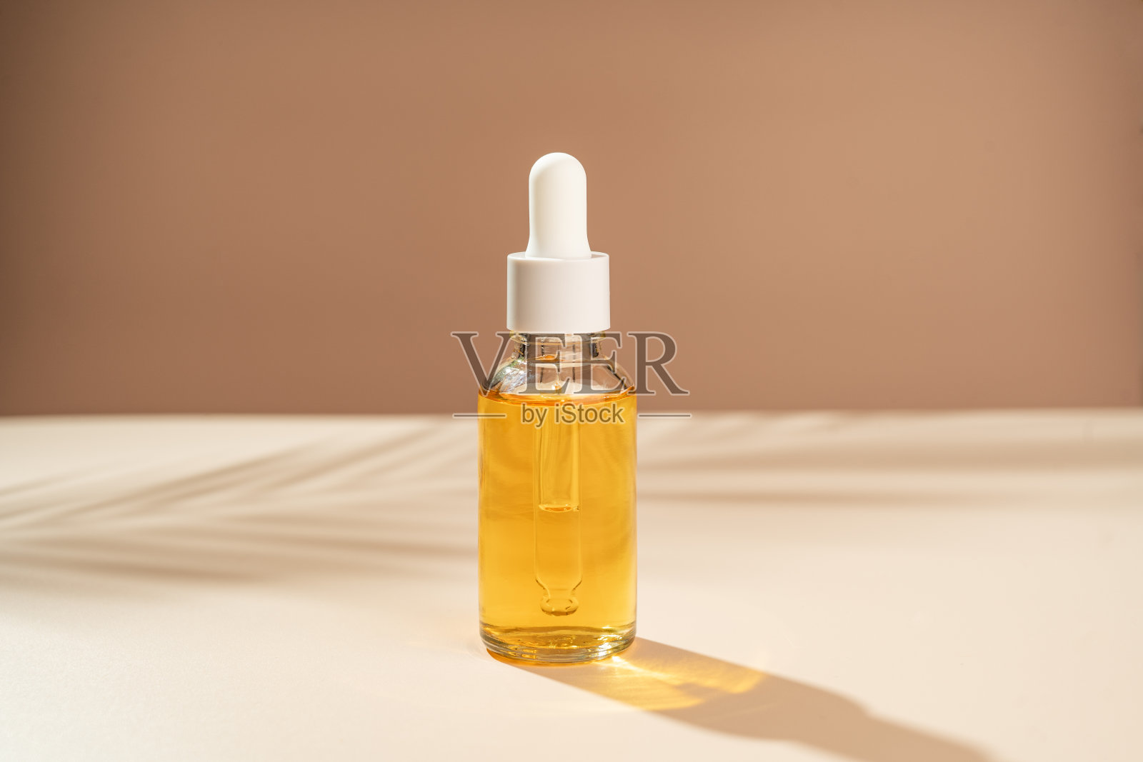 一个黄色的维生素C血清滴管放在桌子上，背景是手掌的阴影。照片摄影图片