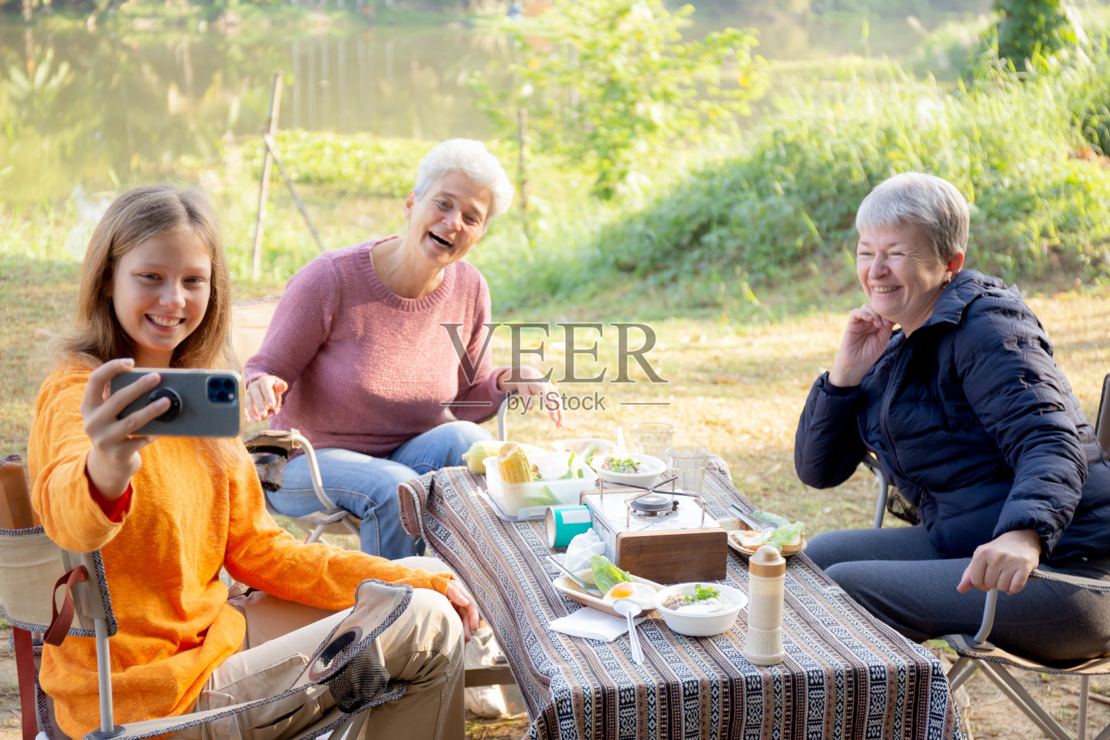 两名老年妇女和青少年在露营时聊天和自拍，在周末早上一起吃早餐时活动娱乐和休闲野餐，在假期旅行。照片摄影图片