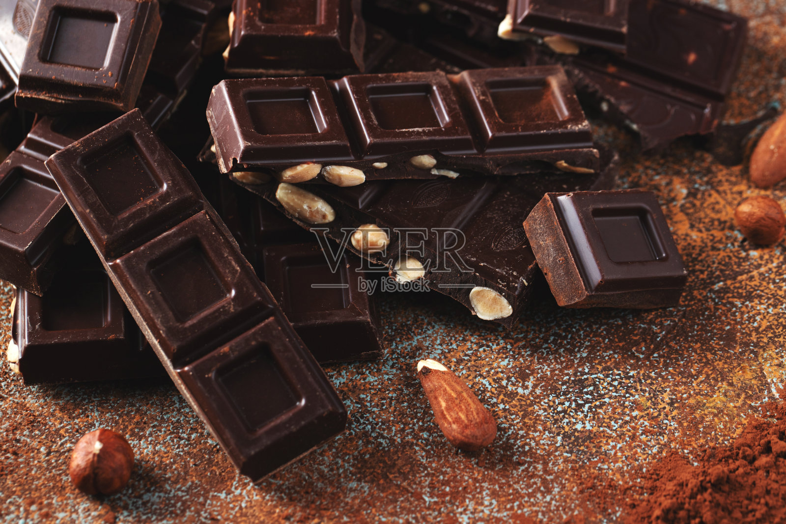 黑牛奶巧克力，黑色背景上撒有可可粉的坚果。照片摄影图片