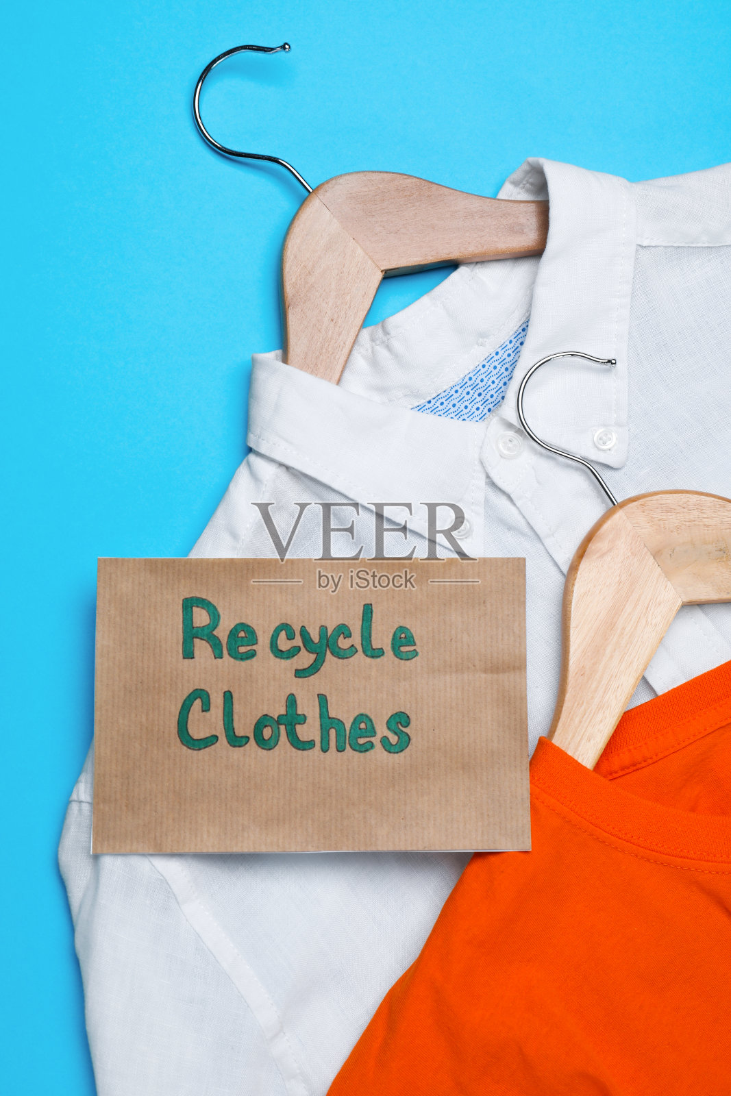 不同的衣服与回收标签和衣架在浅蓝色背景，平铺照片摄影图片