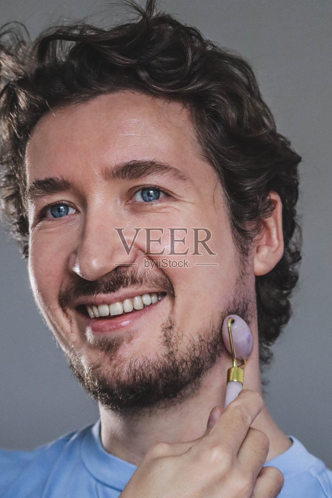 英俊的年轻人按摩他的脸与玫瑰石英辊照片摄影图片