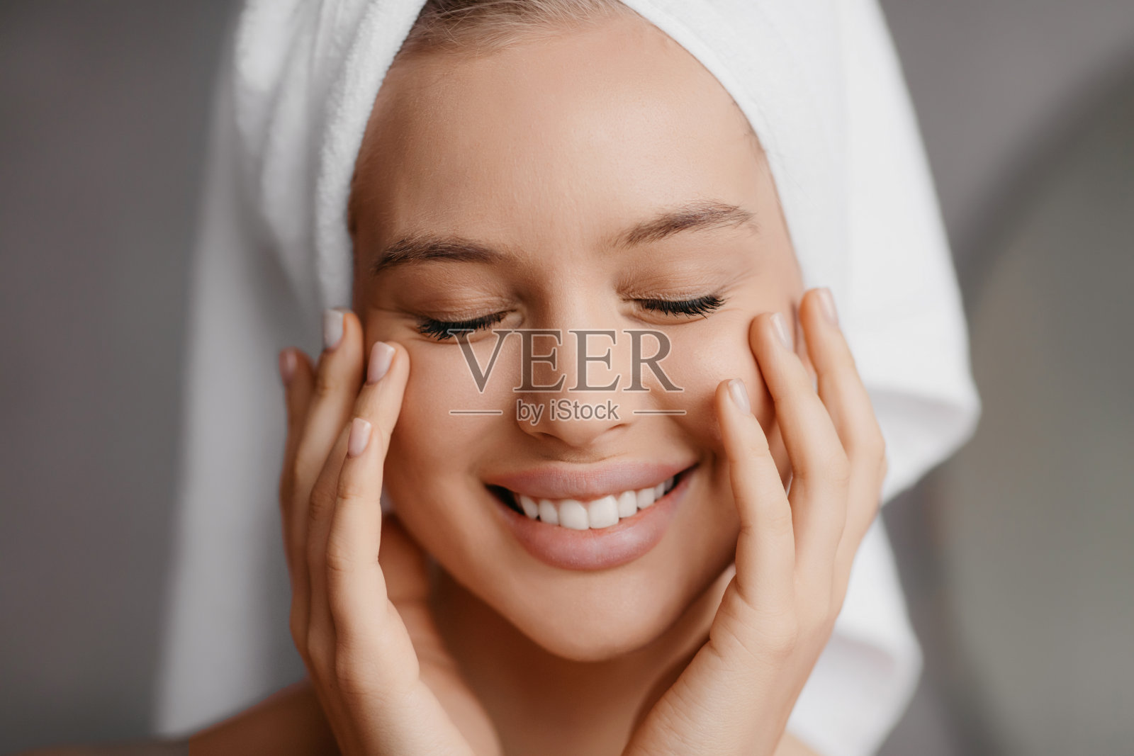 光亮肌肤和水疗护理。微笑的女士在毛巾触摸完美的脸与手，闭着眼睛摆姿势照片摄影图片