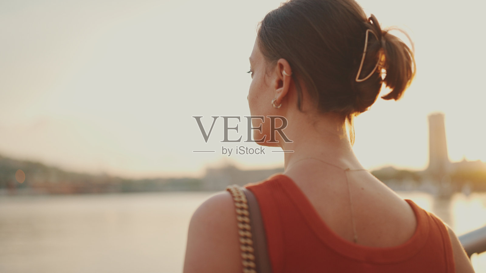 女孩站在河堤上看着海湾。年轻女子在早晨看着大海。后视图照片摄影图片