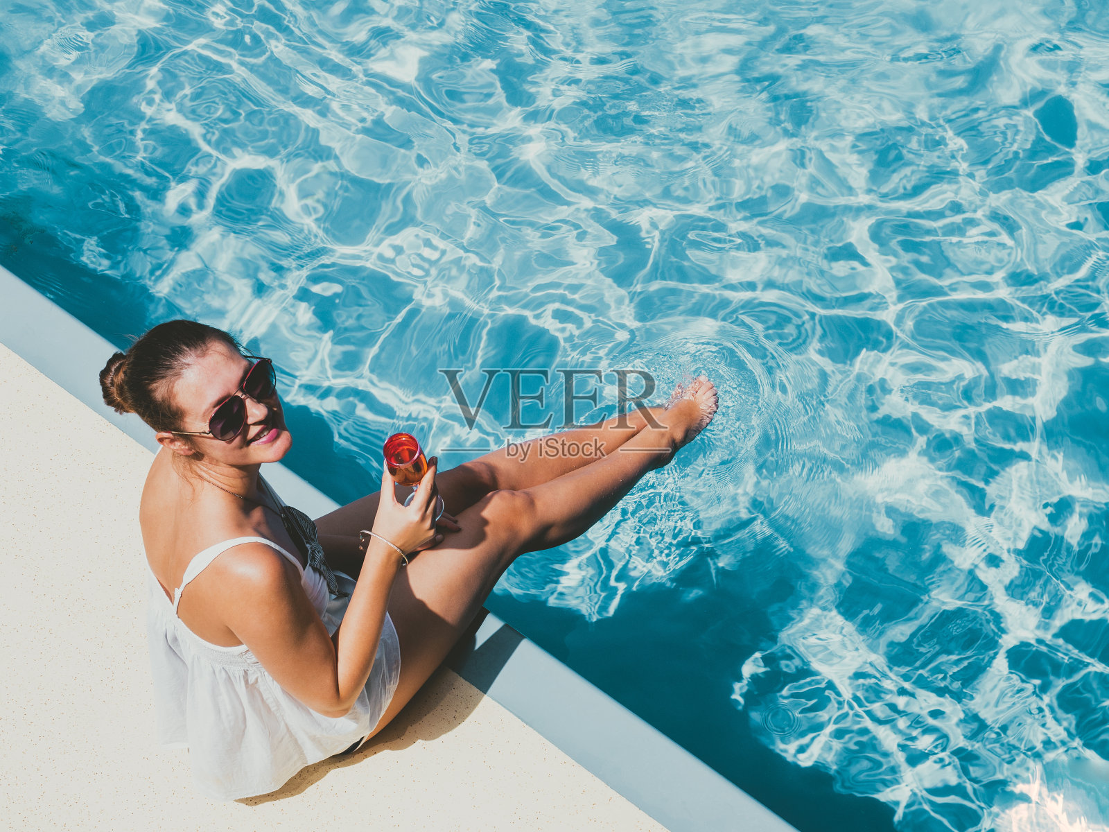 一个时髦的女人坐在泳池边的空甲板上照片摄影图片