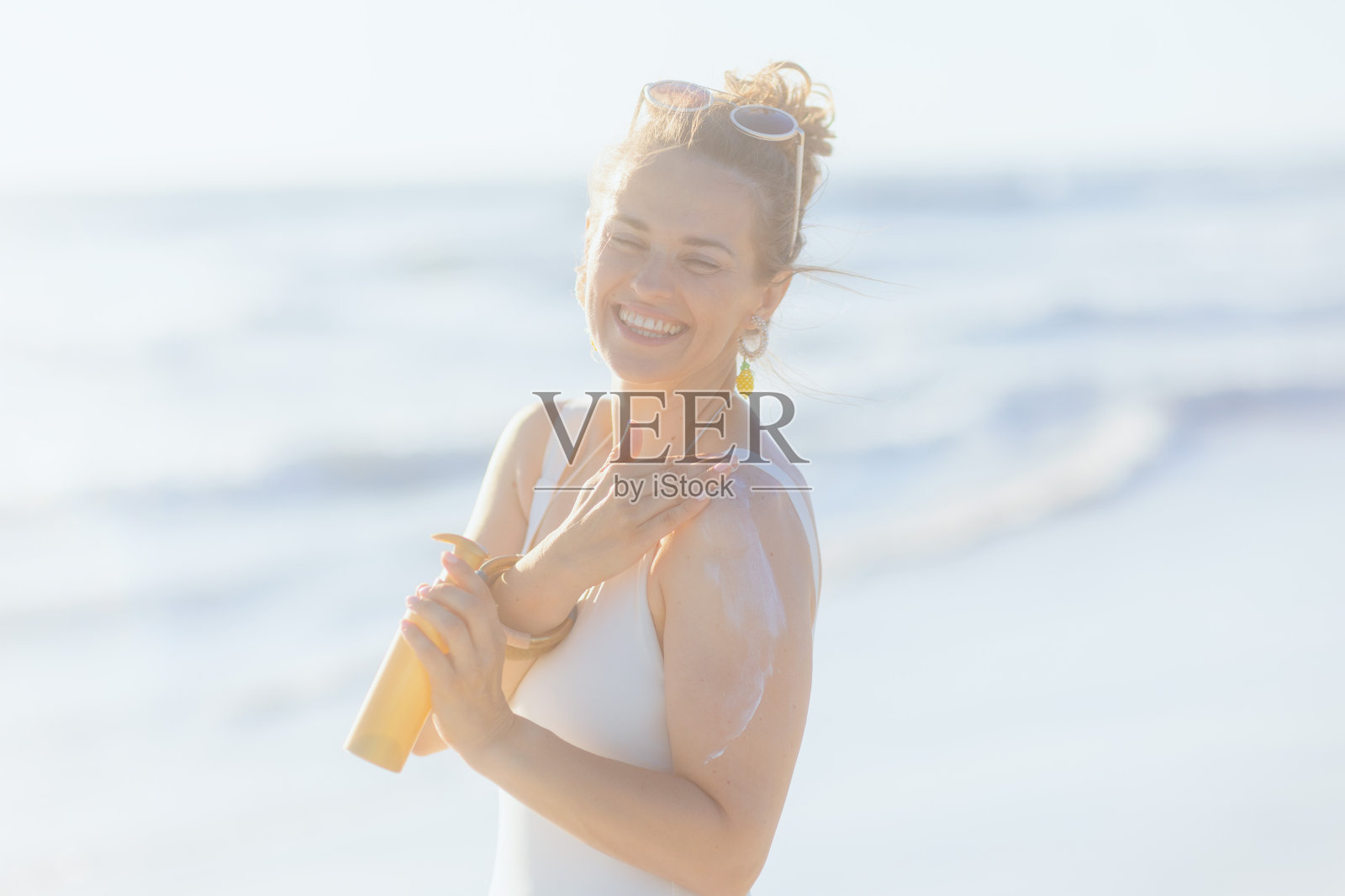 快乐的时尚女子在白色泳衣在海滩使用防晒霜照片摄影图片