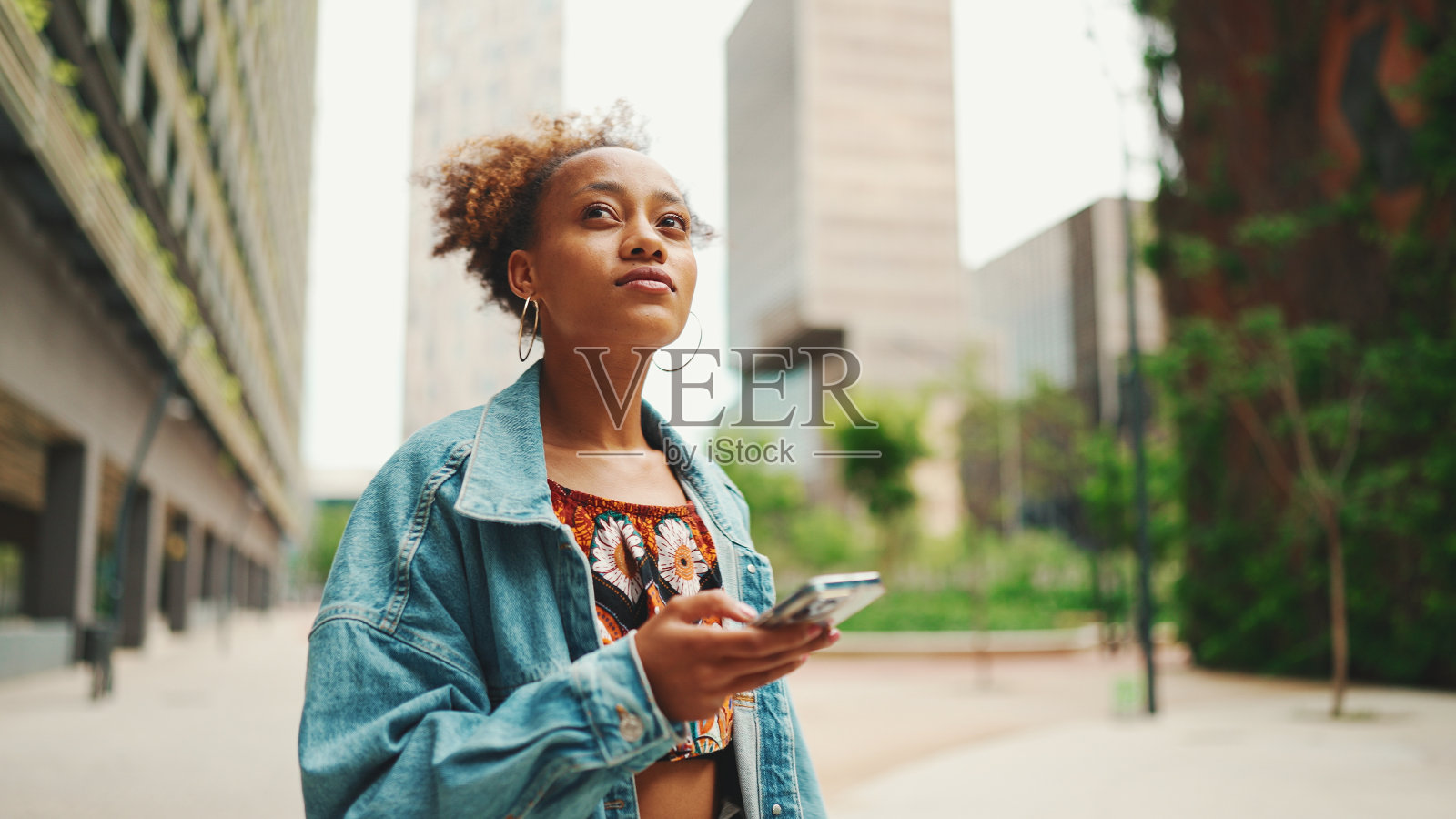 特写非洲女孩穿着牛仔夹克，民族图案的露脐上衣走在现代城市的街头，拿着智能手机看着手机屏幕，在城市里用电子地图寻找地址照片摄影图片