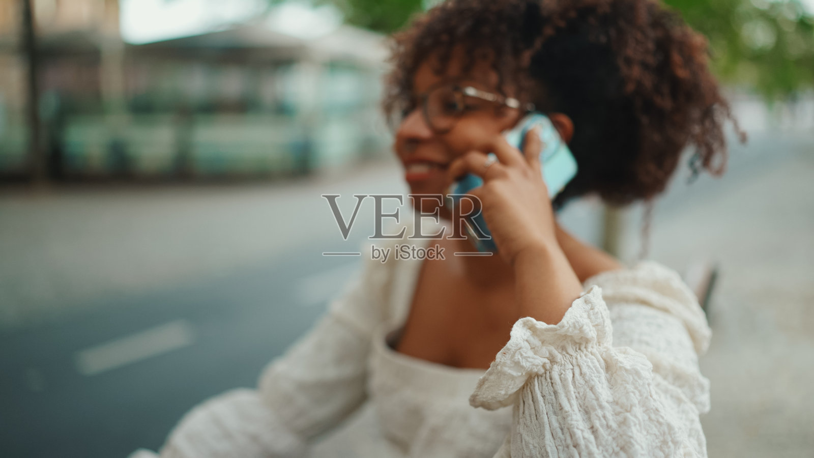 戴眼镜的年轻女人坐在户外长椅上微笑着用智能手机讲话照片摄影图片