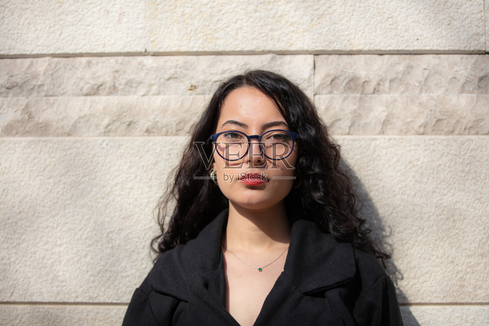 年轻女子站在白色石墙前的肖像。照片摄影图片