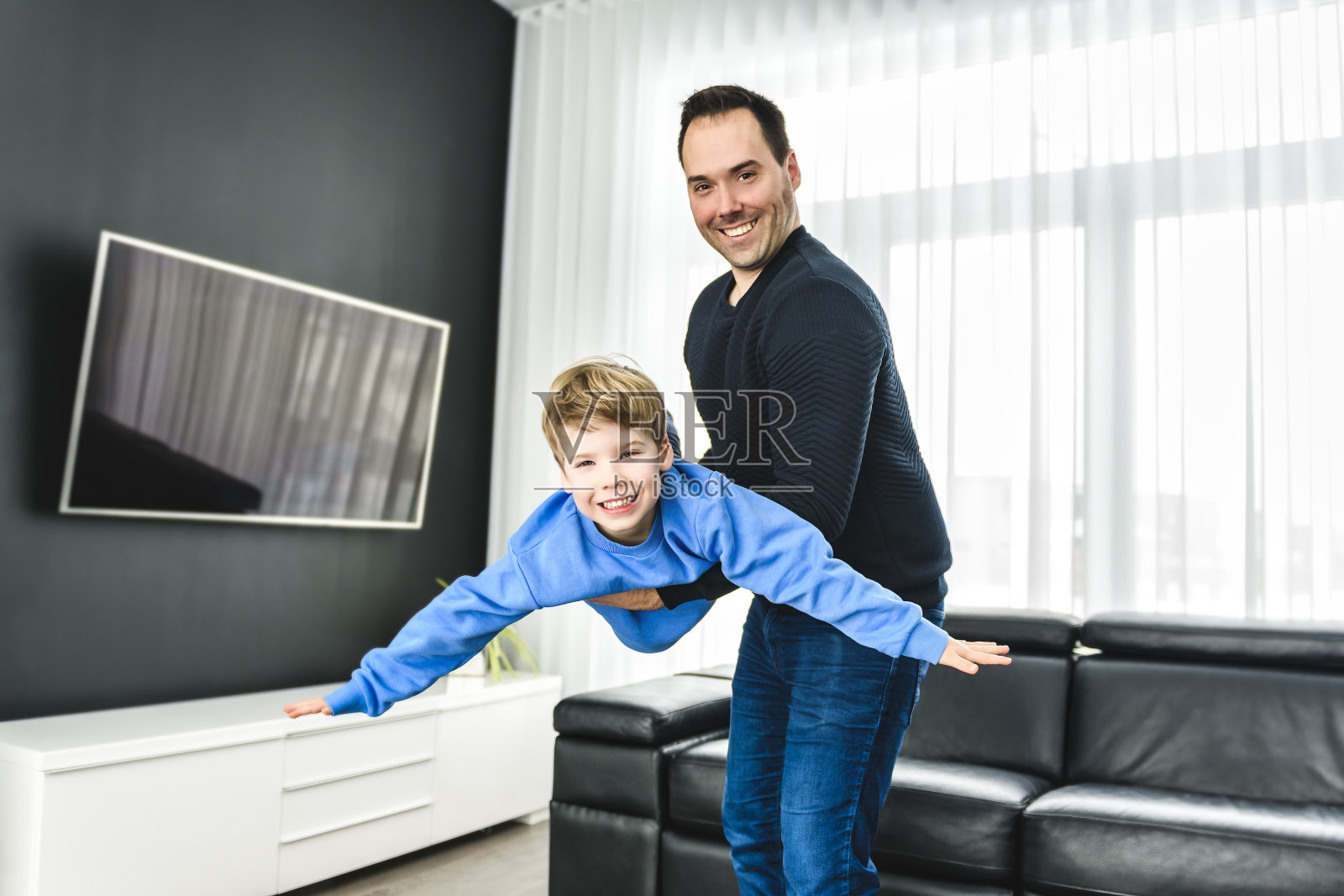 爸爸和他可爱的小男孩在一个现代的房子在客厅玩飞机照片摄影图片