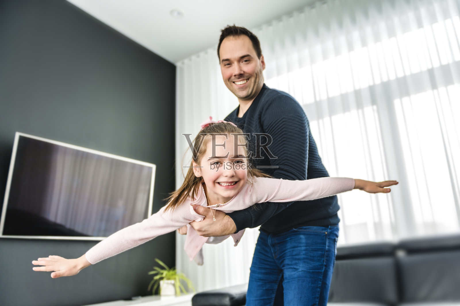 爸爸和他可爱的小女儿在一个现代化的房子里，在客厅玩飞机照片摄影图片