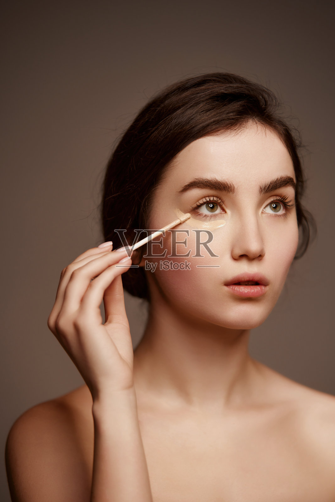 年轻美丽的女孩的肖像，棕色头发，在深灰色的工作室背景下使用遮瑕膏。自然美、护肤、美容的理念照片摄影图片