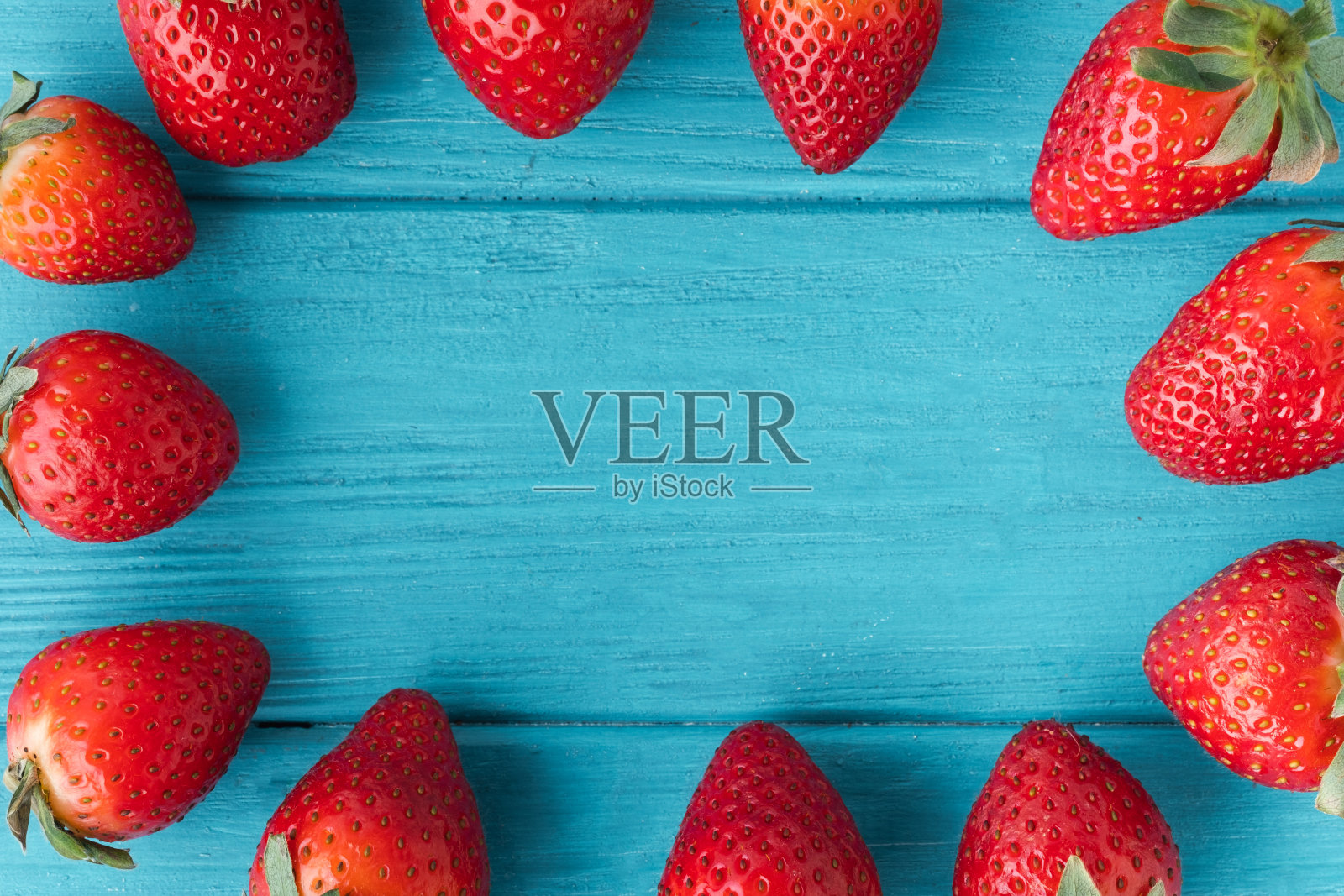 顶部视图的新鲜的红色草莓在木制蓝绿色背景与一个复制空间的自由文本。夏天浆果纹理背景。平躺照片摄影图片